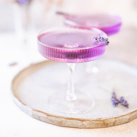 Two purple lavender martinis garnished with lavender on a serving tray