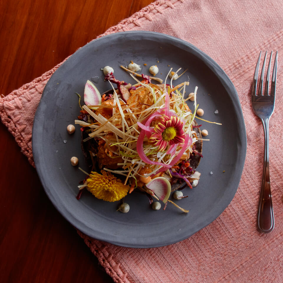 A plate of food on a pink tablecloth on a wooden table with a fork next to it