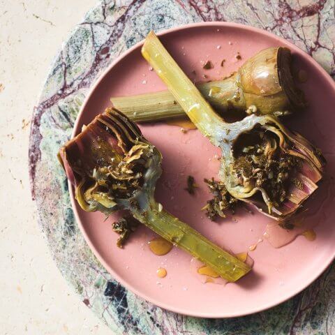 A pink dish with Roman-style artichokes on a marble table.