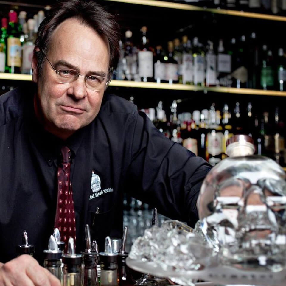 Dan Aykroyd standing behind a bar with a bottle of Crystal Head vodka