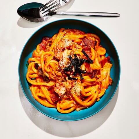 A blue bowl with noodles and a fork and spoon next to it