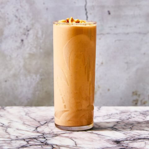 A glass of peanut punch on a marble surface with a concrete wall behind it