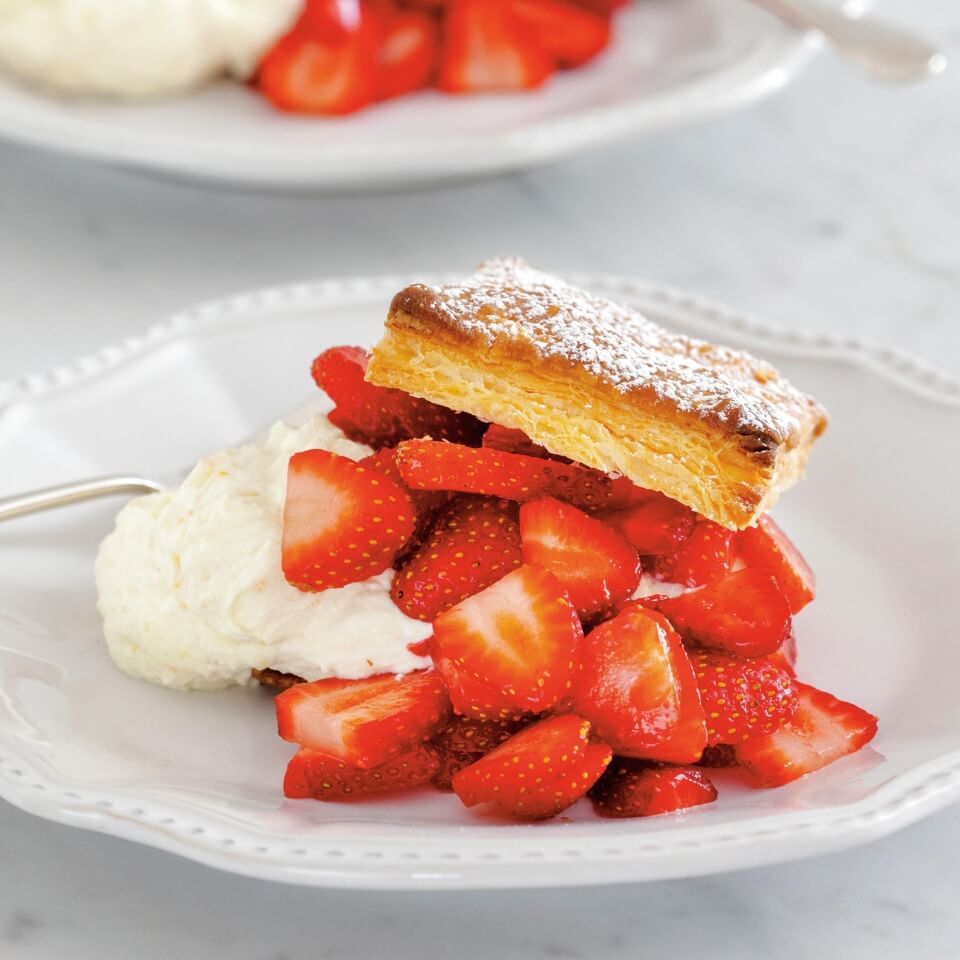 Strawberry Napoleons on white dessert plates, puff pastry layers dusted with icing sugar and fresh strawberries