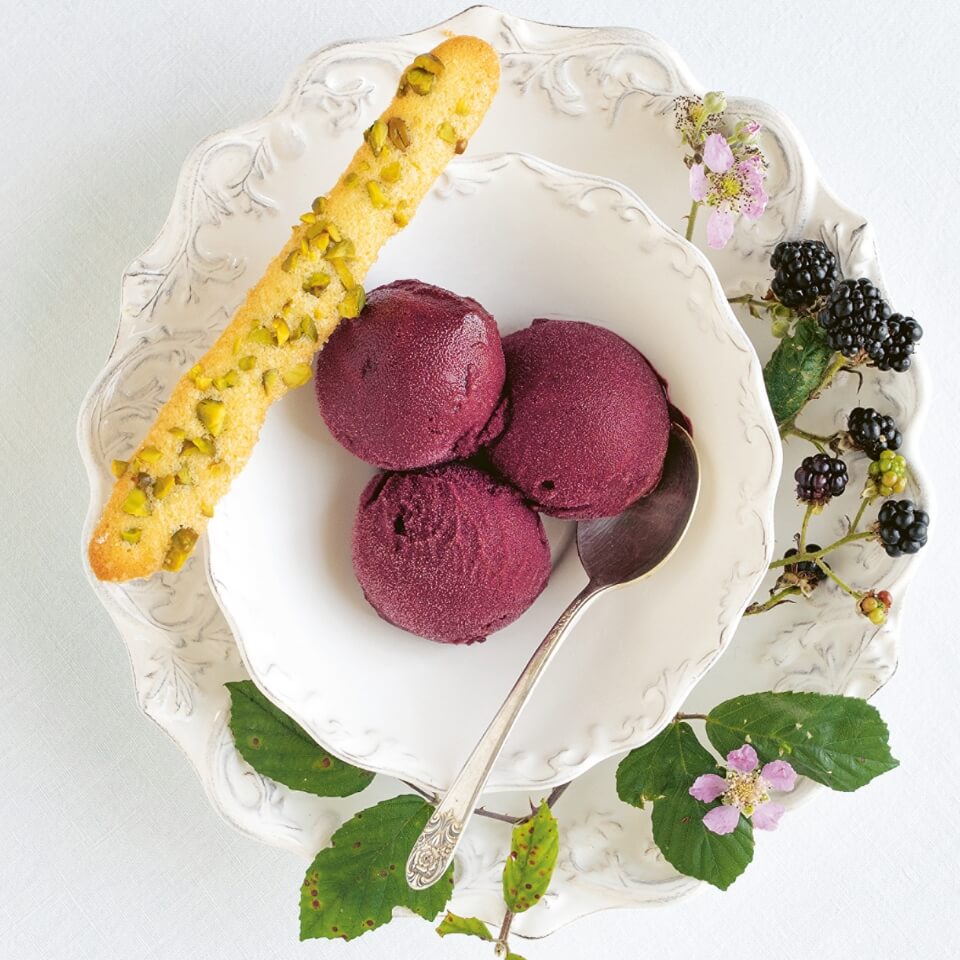 A white bowl of blackberry sorbet with a biscuit