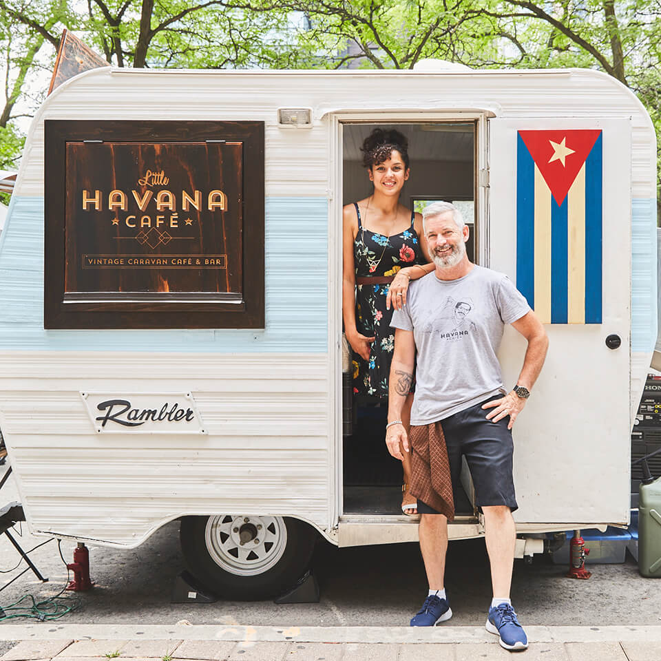 Two people standing with a small white-and-blue trailer