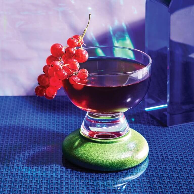 A cocktail garnished with grapes against a blue and purple background