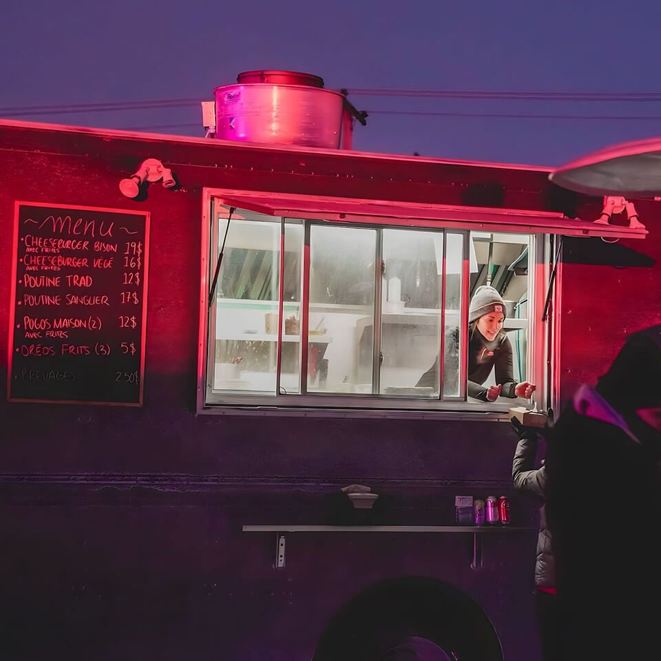 A person passing food to a customer out the window of a black food truck with a chalkboard menu at nighttime