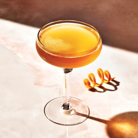 A Sidecar cocktail in a couple glass with an orange rind twist next to it
