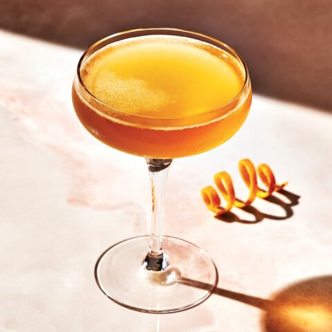 A Sidecar cocktail in a couple glass with an orange rind twist next to it