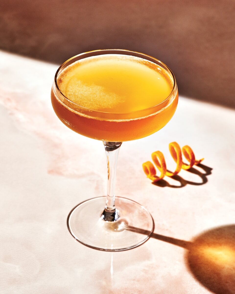 A Sidecar cocktail in a couple glass with an orange rind twist next to it