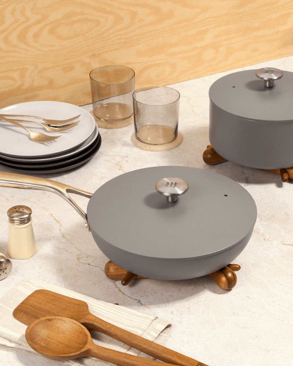 two grey pots sitting on a countertop with glasses and serving cutlery