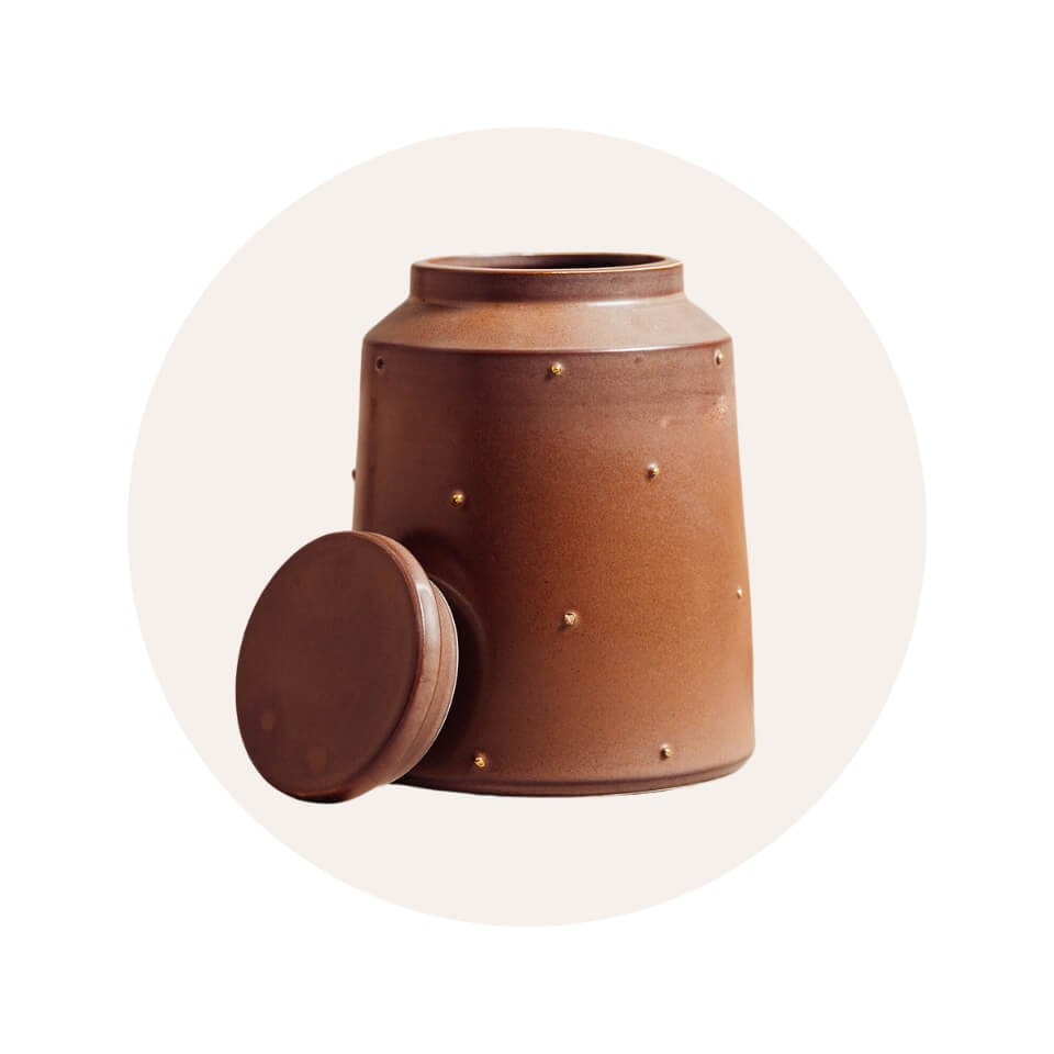 A brown ceramic cookie jar with circular gold accents and the lid by its side in a cream-coloured circle