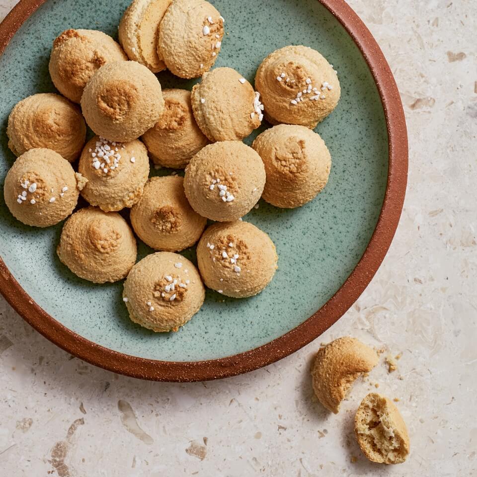 A turquoise-and-brown dish with crisp Italian amaretti cookies on a countertop and a broken one next to it