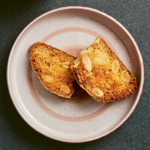 A pink plate with an almond cookie broken in half Cantucci Italian almond biscotti broken in half on a plate