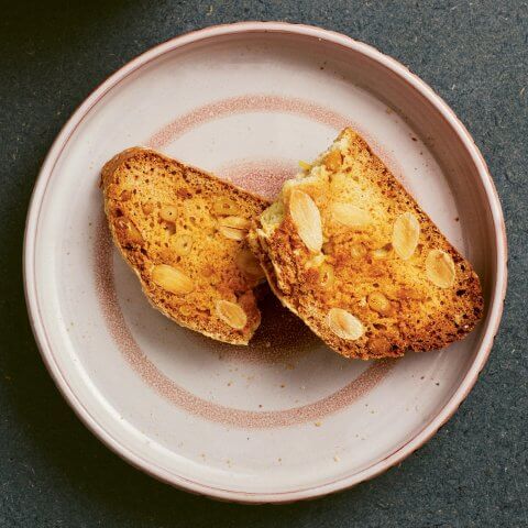 A pink plate with an almond cookie broken in half Cantucci Italian almond biscotti broken in half on a plate