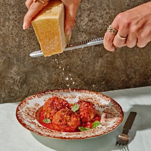 A person grating cheese over a dish with three meatballs