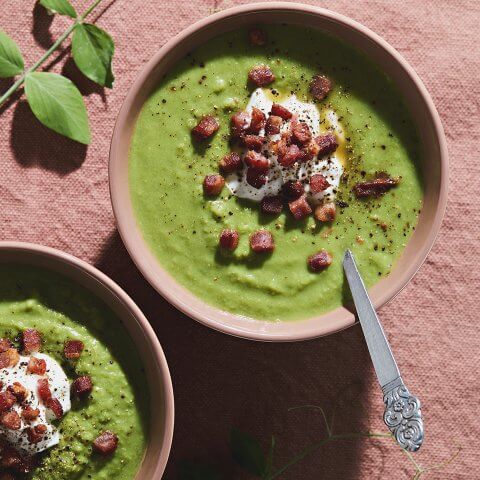Two bowls of pea soup on a reddish tablecloth