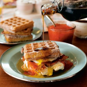 Syrup being poured over a waffle breakfast sandwich