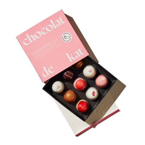 A pink box opened to show nine chocolate truffles.