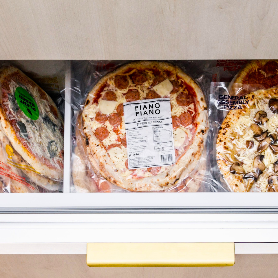 Open freezer drawer with frozen pizzas by Canadian companies inside