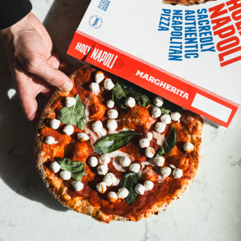 Hand pulling frozen pizza out of takeout box that says Holy Napoli, a Canadian company