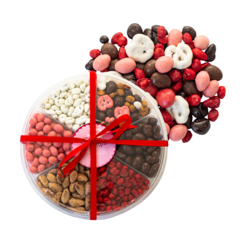 Circular platter filled with six different nuts and snacks with a pile of yogurt-covered pretzels and nuts.