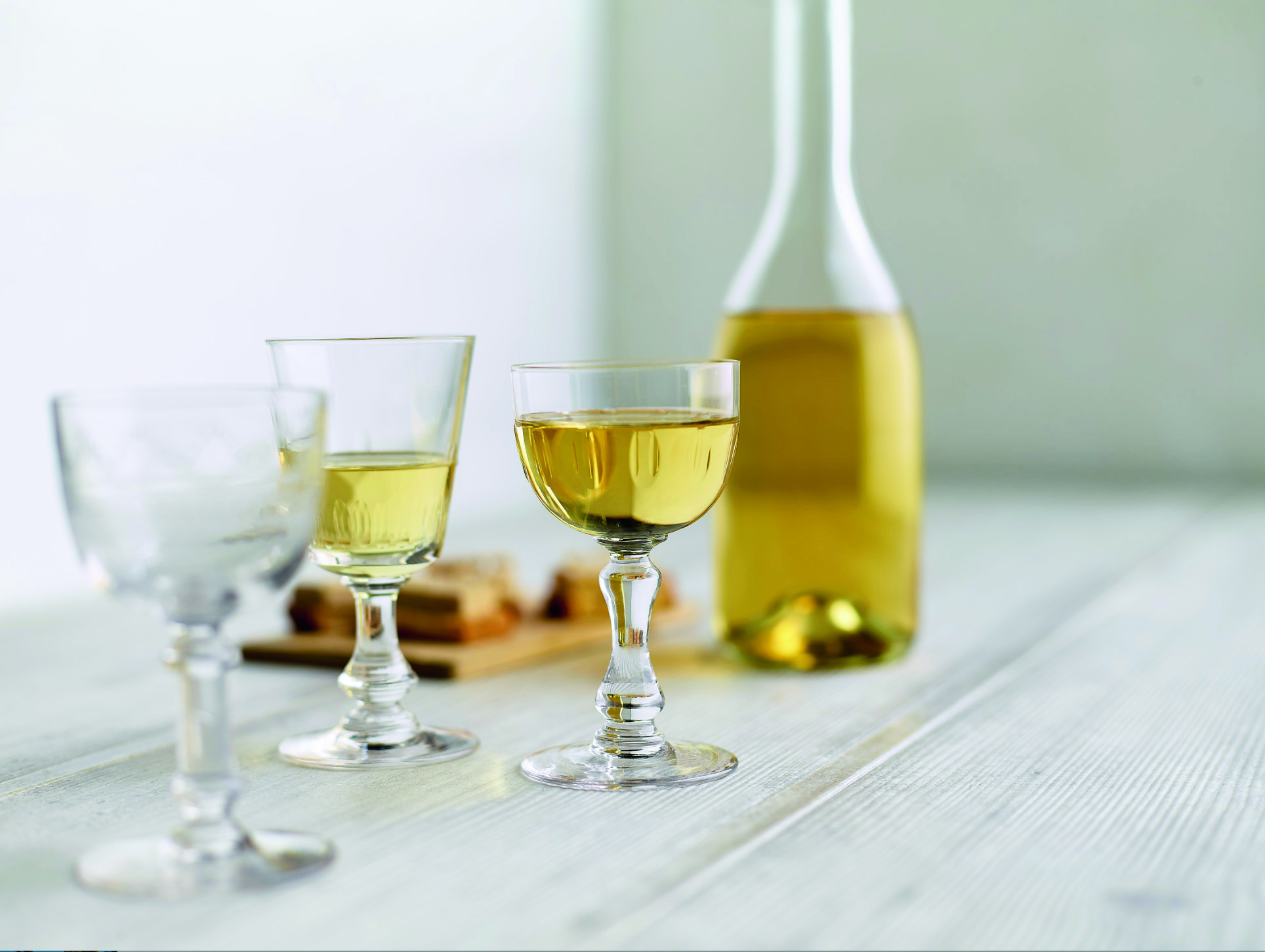 A carafe of Hungarian Tokaj – a beautifully made dessert wine, is sitting on a white table with stemmed glasses.