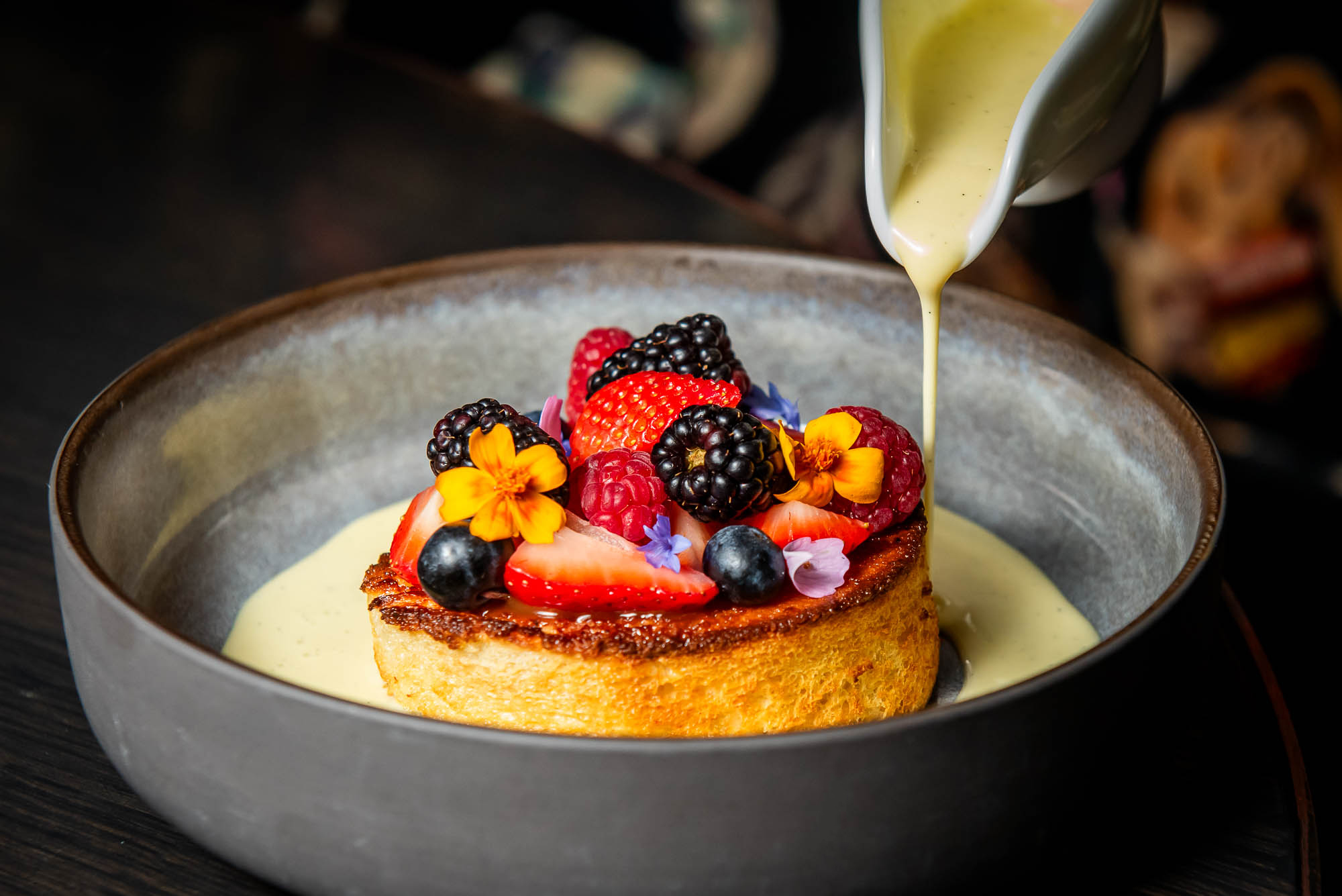 Custard poured around a circular toast topped with berries and flowers.