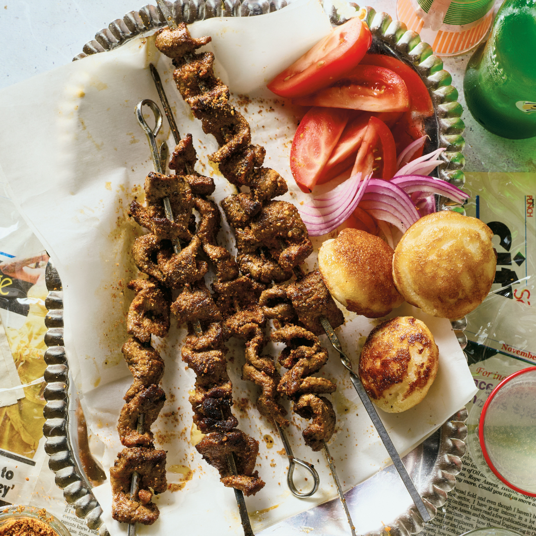 Beef suya skewers on a dish with tomato slices, red onion slices.