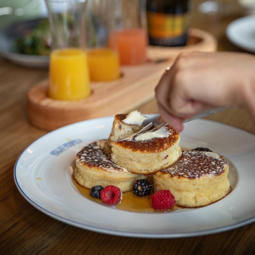 A soufflé pancake being sliced in half atop two other pancakes. 