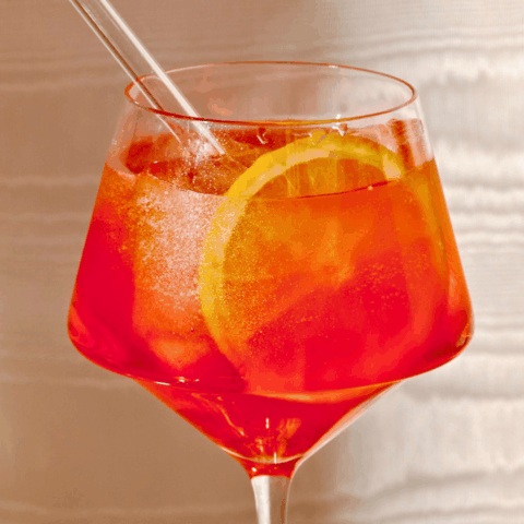 Close-up of an Aperol Spritz in a crystal glass with ice cubes and slice of lemon.