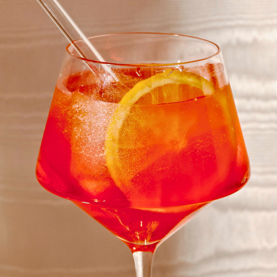 Close-up of an Aperol Spritz in a crystal glass with ice cubes and slice of lemon.