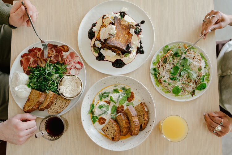 Four plates of brunch foods on a light wood table.