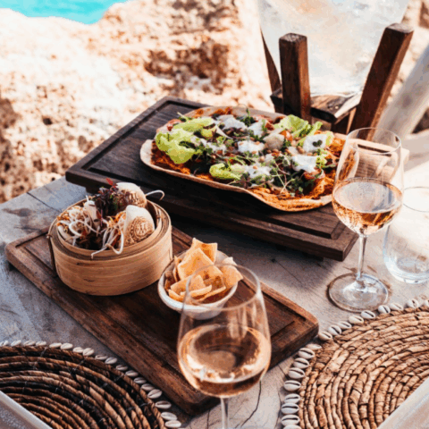 Dining by the water at Mood Beach, Curaçao with glasses of rose, flatbread pizza and woven placemats