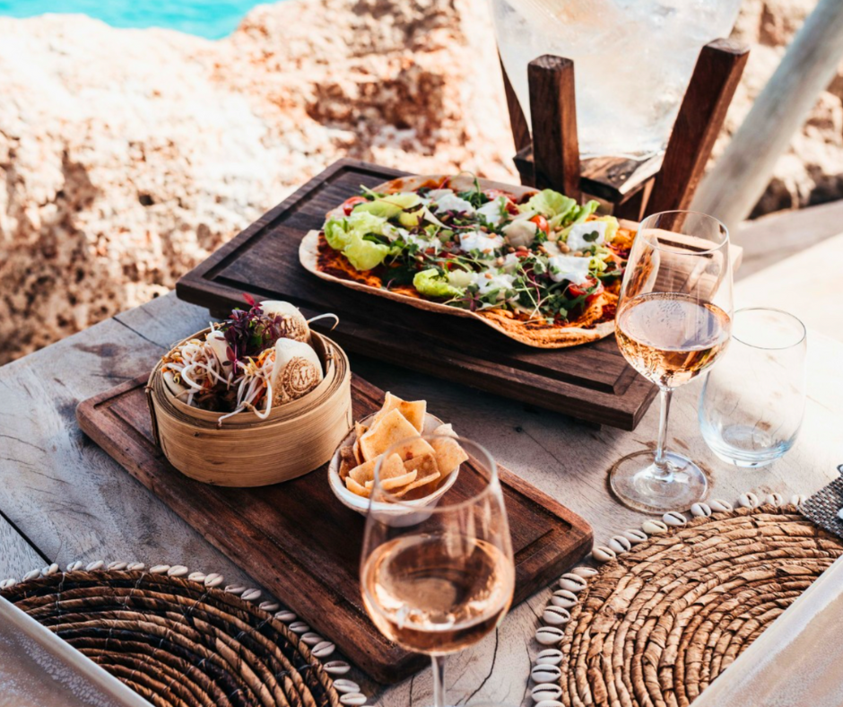 Dining by the water at Mood Beach, Curaçao with glasses of rose, flatbread pizza and woven placemats