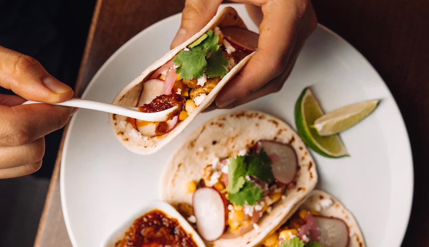 A hand holding a taco while chili oil is spooned on top. 