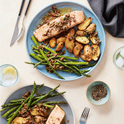 two plates of a healthy dinner which includes salmon, asparagus and roasted potatoes