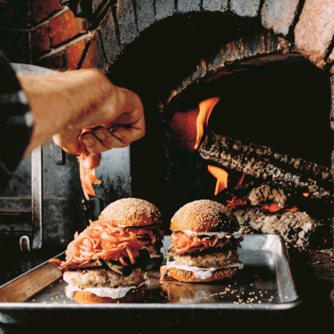 Salmon burgers on a metal tray in front of a wood burning fire