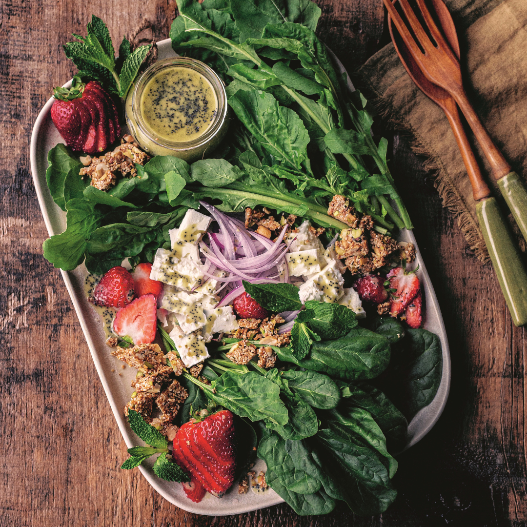 Long plate piled with spinach, arugula, feta, strawberry and red onion with a small bowl of creamy dressing
