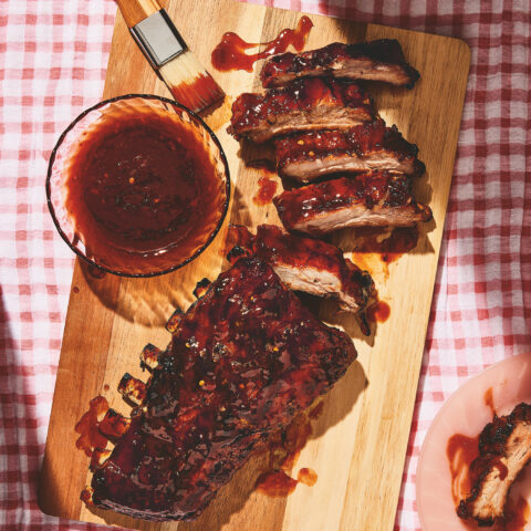 Best Barbecue Ribs Recipe from Dolly Parton with barbecue sauce on the side. Ribs aresitting on a wooden board