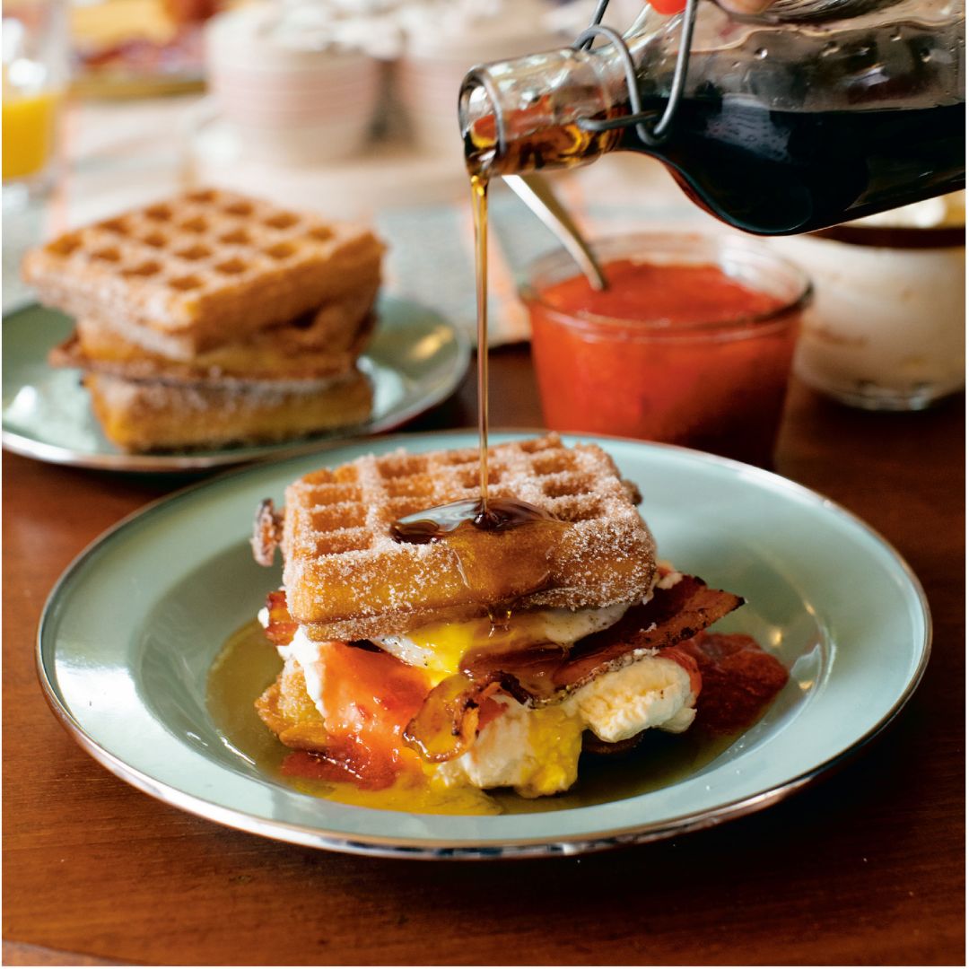 Maple syrup being poured onto a waffle sandwich with egg and bacon. Recipe from Matty Matheson's cookbook