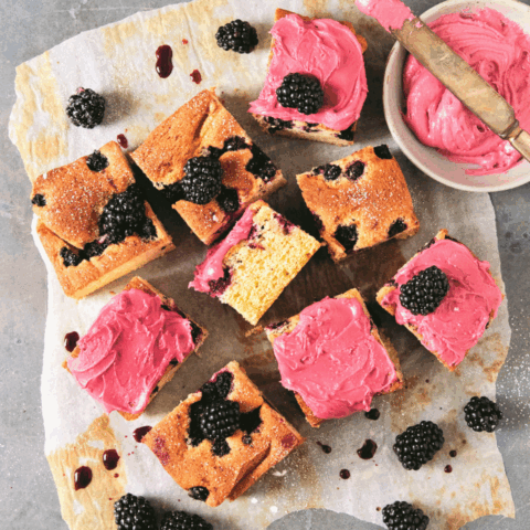 Overhead shot of Blackberry Almond Snacking cake recipe cut into squares with pink frosting.