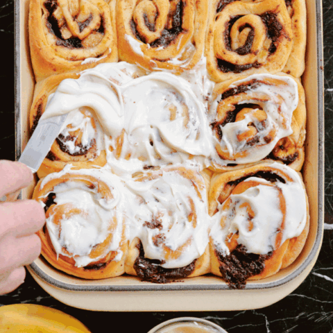 Cream cheese frosting is spread overtop a spread on top of chocolate banana swiirod