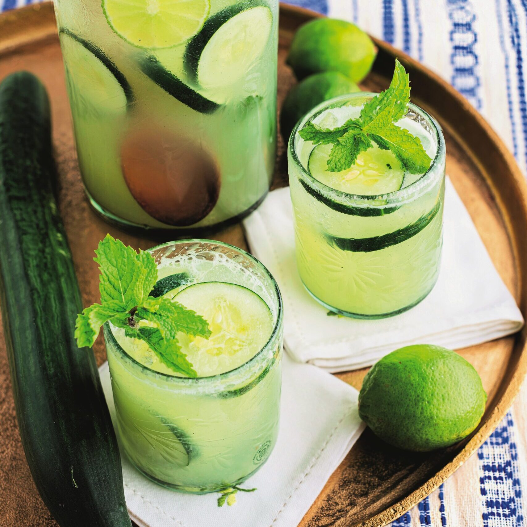 One pitcher and two glasses filled with cucumber lime agua fresca on a brown platter.