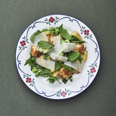 White plate with red decorative flowers on the edge topped with potato salad and halloumi.