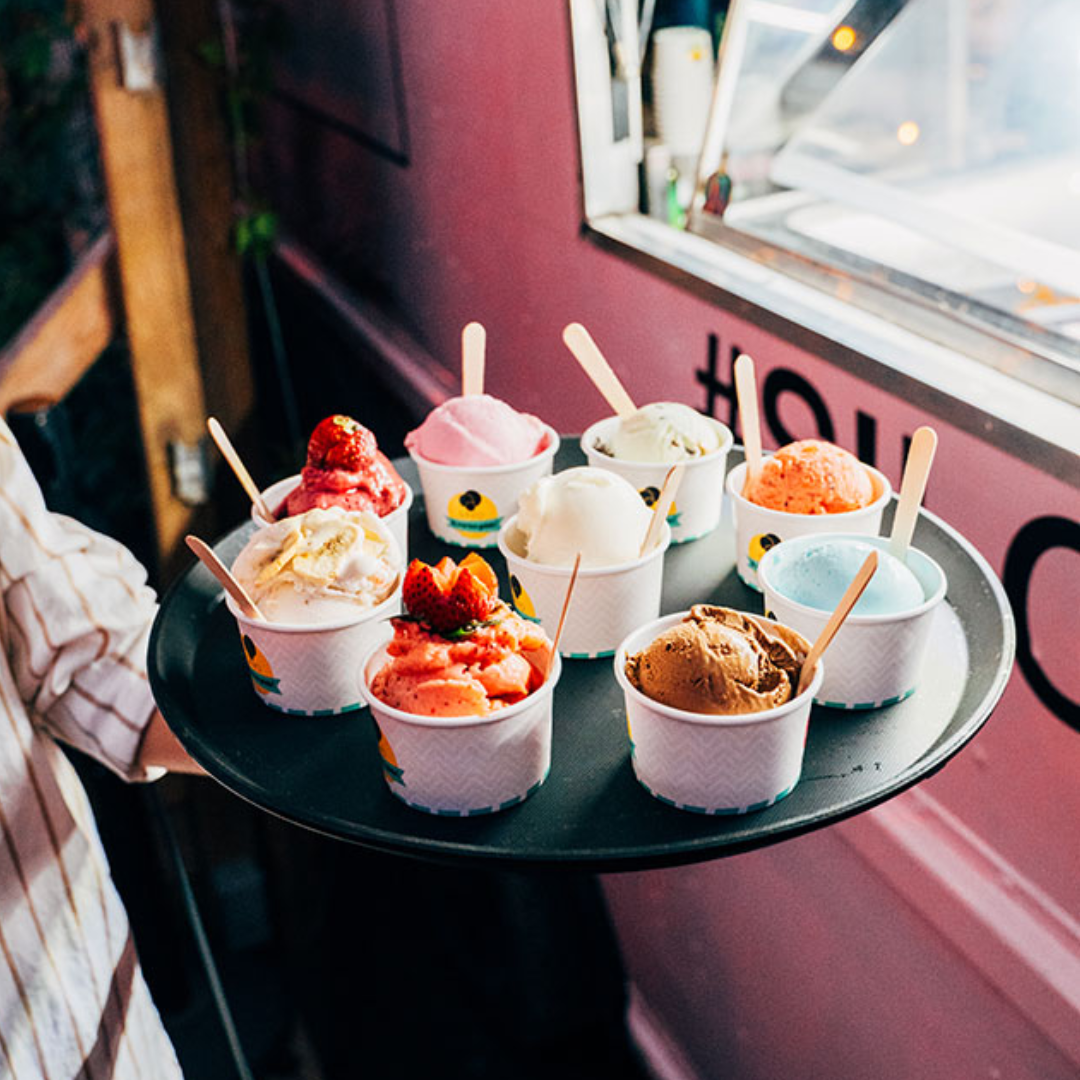 A platter topped with scoops of ice cream in little cups in front of a pink ice cream truck.