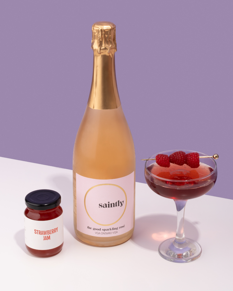 A bottle of Canadian Saintly The Good Sparkling Rosé with a Berry Fizz Rosé cocktail with raspberries and jam