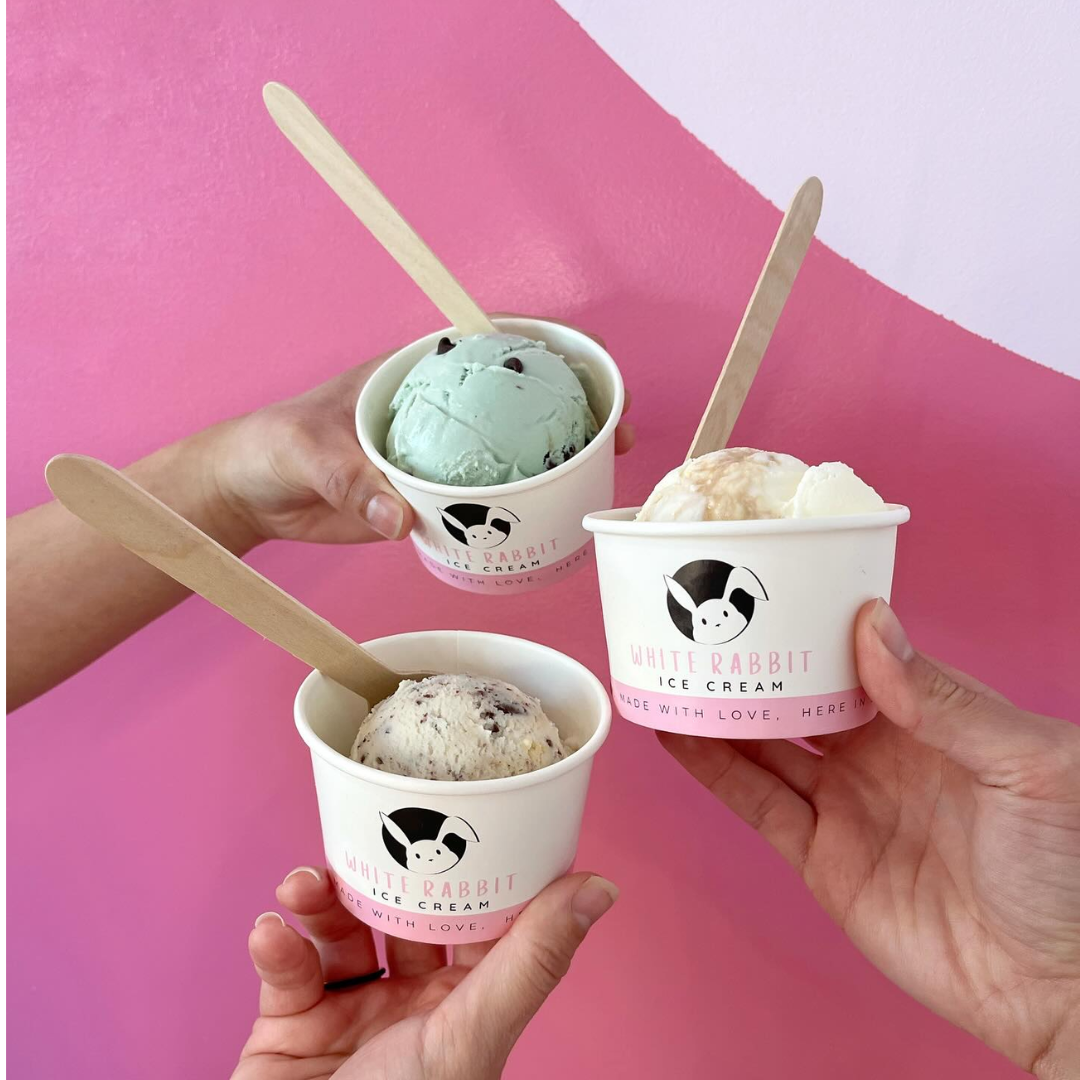 Three cups of ice cream in front of a pink and white wall.