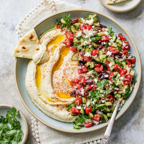 A bowl of Mediterranean hummus salad with a slice of pita bread.