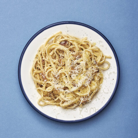Vegetarian spaghetti carbonara on a white plate on a blue background.